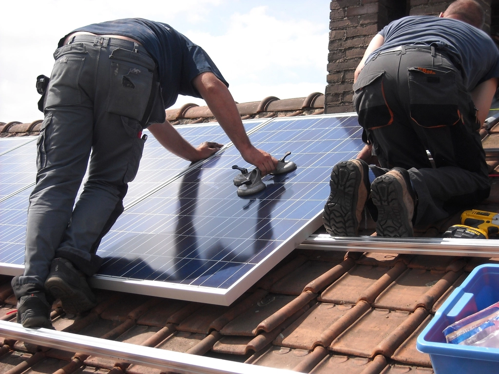 Installers fitting solar panels to a pitched roof on a UK house