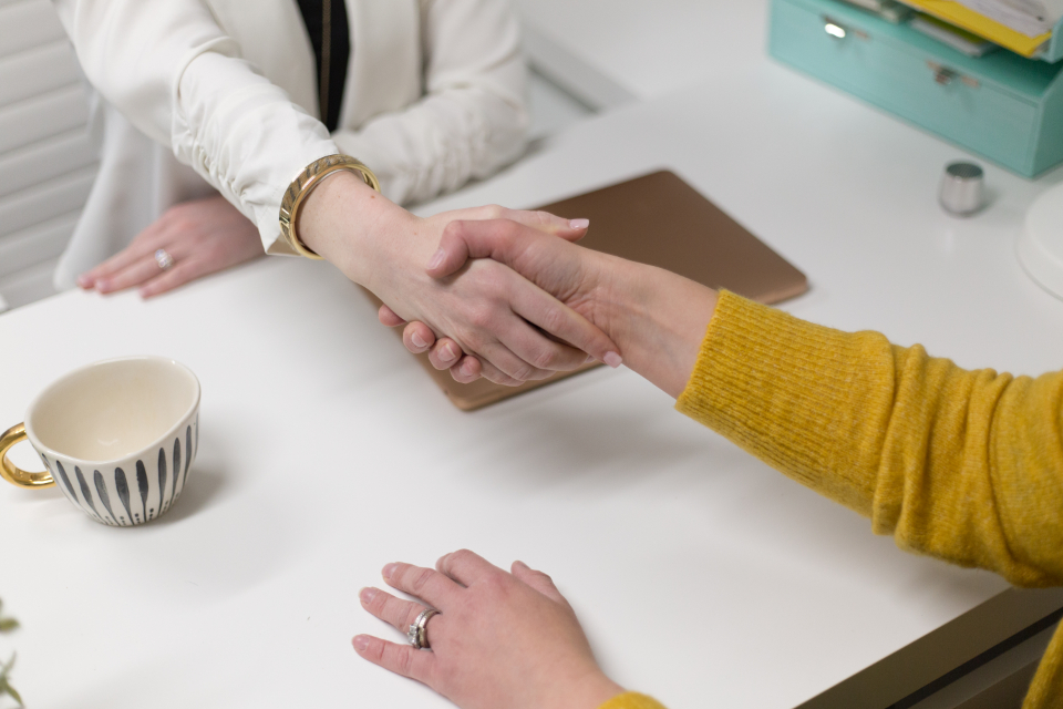 Two people shaking hands across a desk in an office